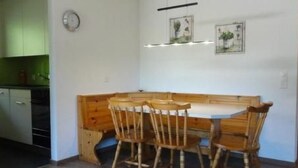 Een eetgedeelte met een houten tafel en stoelen, een klok aan de muur, en ingekaderde foto's erboven.