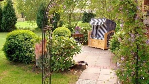 En trädgård med en trästol och ett bord under en pergola som är översållad med lila blommor.