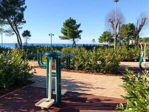 Ein Trainingsbereich im Freien mit einer Bank und einer Handläufe, umgeben von Grünflächen und Meerblick.