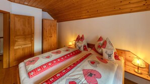 Ein Schlafzimmer mit Holzboden, einem Bett mit rot-weißer Bettwäsche und einer Nachttischlampe.