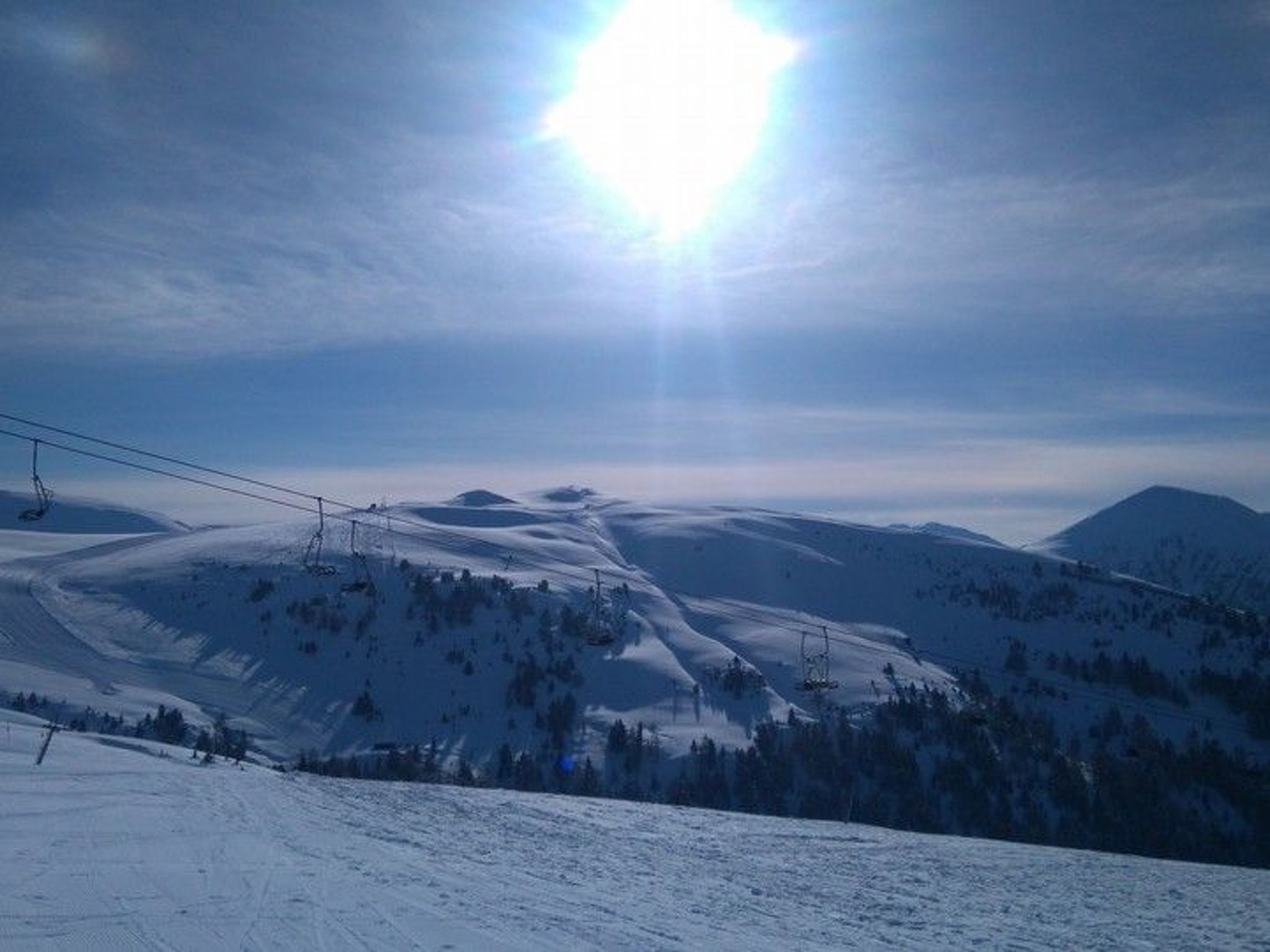 Un paysage de montagne enneigé, avec des remontées mécaniques et un ciel dégagé.