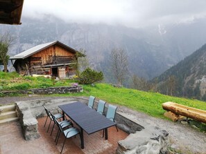 A rustic wooden cabin with a stone patio and outdoor seating area, surrounded by lush greenery and mountains. - Husmättli by Interhome (Lauterbrunnen)