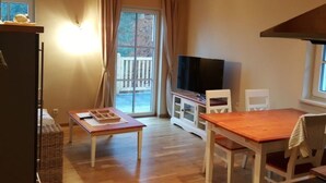A cozy room with a wooden ceiling, a television on a stand, a dining table with chairs, and a large window with curtains. - Villa Albatros in Oberdellach by Interhome (Oberdellach)