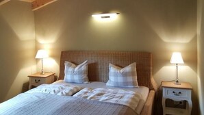 A bedroom with a wooden ceiling, a bed with white bedding, two bedside tables with lamps, and a wall-mounted light fixture. - Villa Albatros in Oberdellach by Interhome (Oberdellach)
