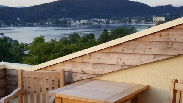 A wooden deck with a table and chairs overlooking a river and hills. - Villa Albatros in Oberdellach by Interhome (Oberdellach)