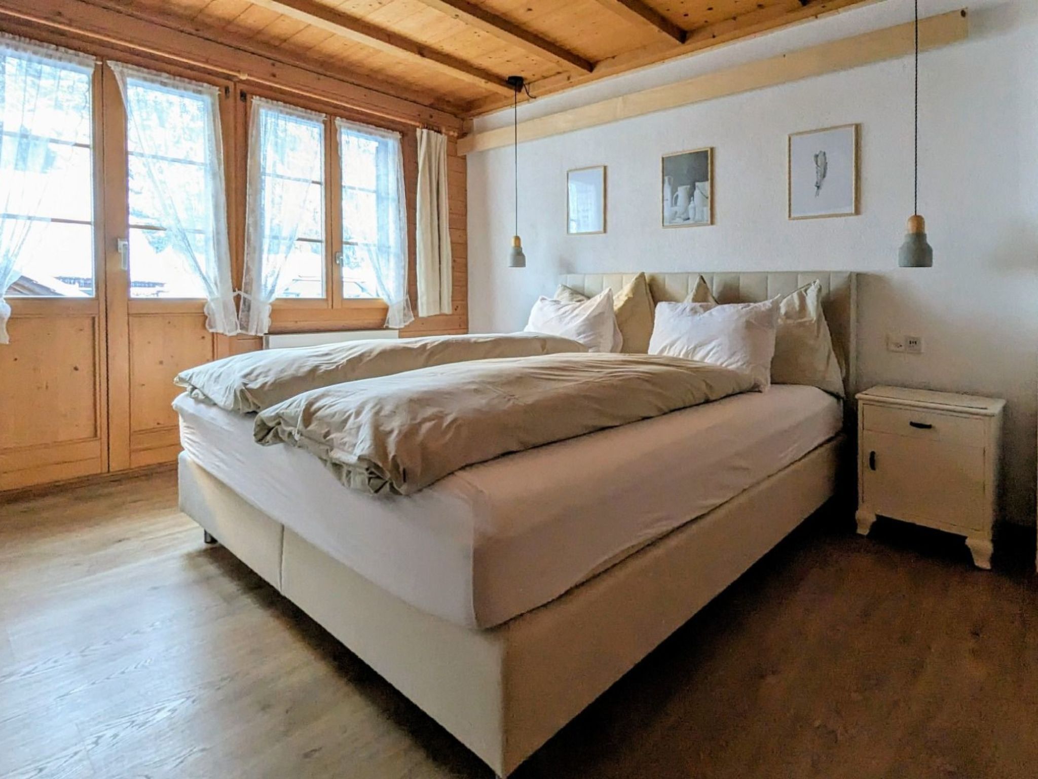 Un dormitorio con una cama grande, pisos de madera, techo de madera y una ventana con cortinas.
