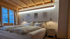 A bedroom with a large bed, a nightstand, and a window with curtains. - Margrit Ost by Interhome (Lauterbrunnen)