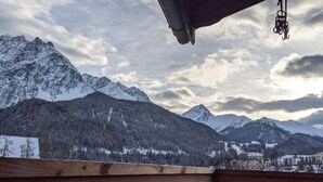 En träbalkong med utsikt över snötäckta berg och en molnig himmel.
