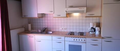 A compact kitchen with white cabinets, a built-in oven, a sink, and a coffee maker.