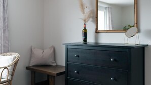 Ein Schlafzimmer mit einer dunklen Holzkommode, einem Spiegel, einer Weinflasche und einer Vase mit getrockneten Blumen.