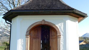 A small chapel with a cross on top, wooden doors, and a gravel path in front. - in Sankt Koloman mit Bergblick by Interhome (St. Koloman)