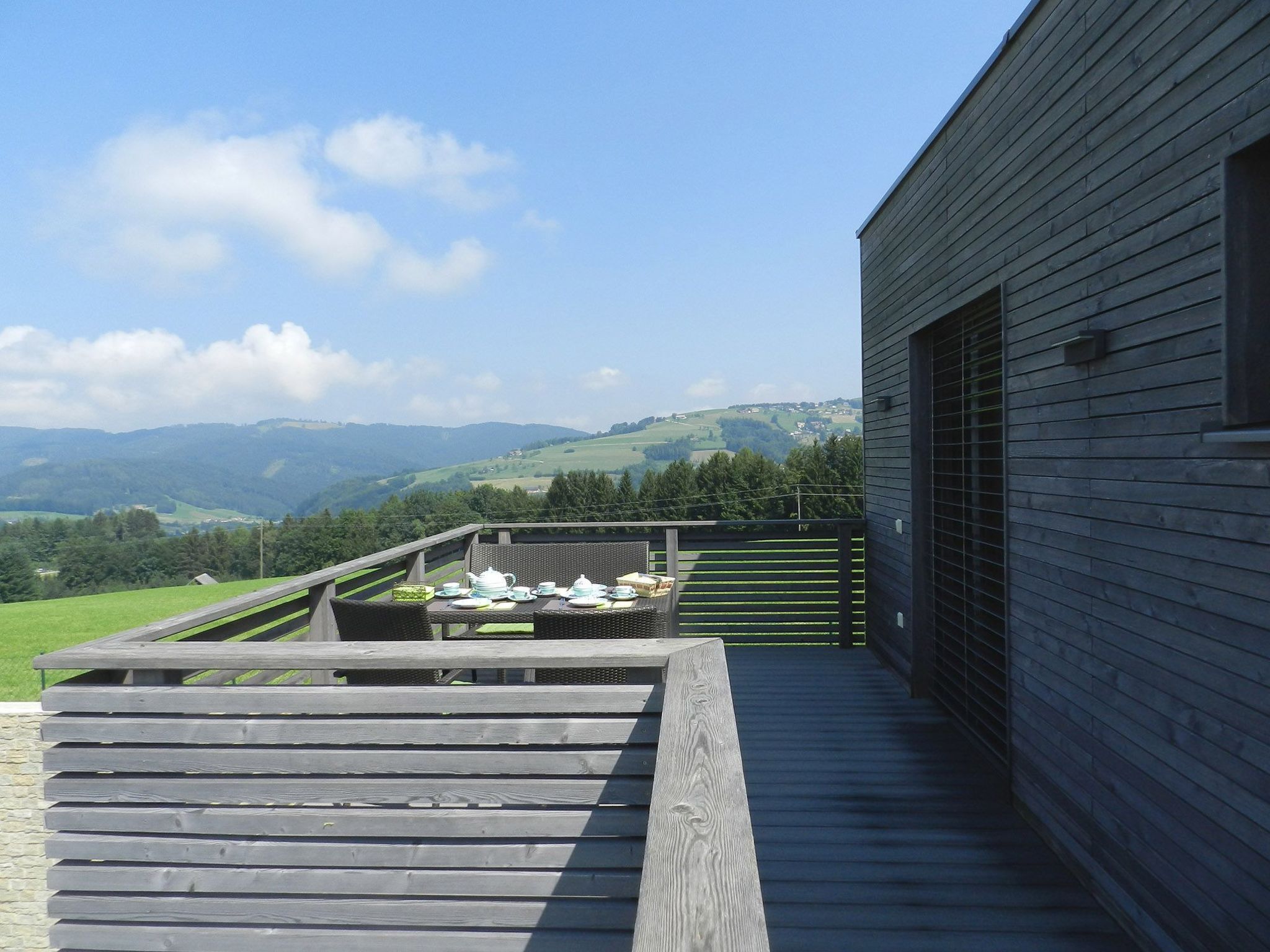 A wooden deck with a table set for tea, overlooking a scenic valley.