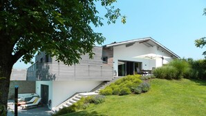 Una casa moderna con un porche cubierto, una escalera que lleva a una terraza y un césped bien cuidado.