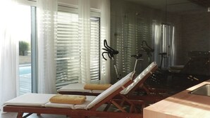 Una habitación moderna con suelo de madera, ventilador de techo, cabina de ducha de vidrio y dos tumbonas.