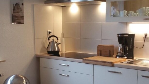 A modern kitchen with white cabinets, a stainless steel kettle, a coffee maker, and a trash can. - Ganze Wohnung in Voslapp by Interhome (Wilhelmshaven)