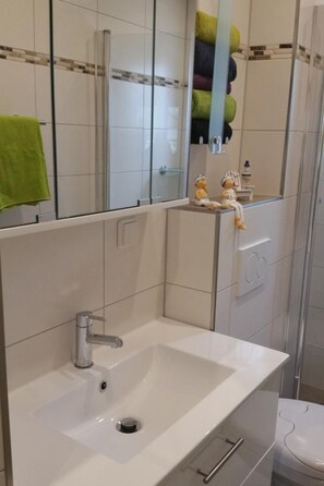 Et badeværelse med hvid vask, spejl og toilet.