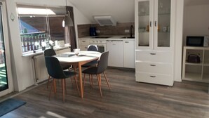 A modern kitchen with a dining area, featuring a round table with chairs, a built-in oven, and a white cabinet with glass doors. - Amselnest by Interhome (Wiesmoor)