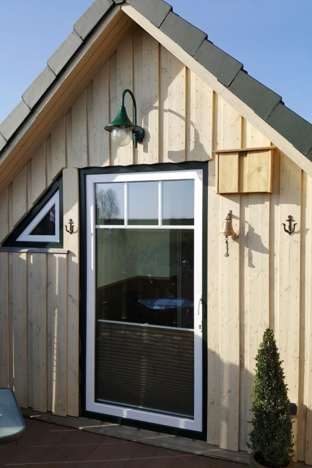 A wooden building with a large window and a door, a small tree, and a light fixture on the roof.