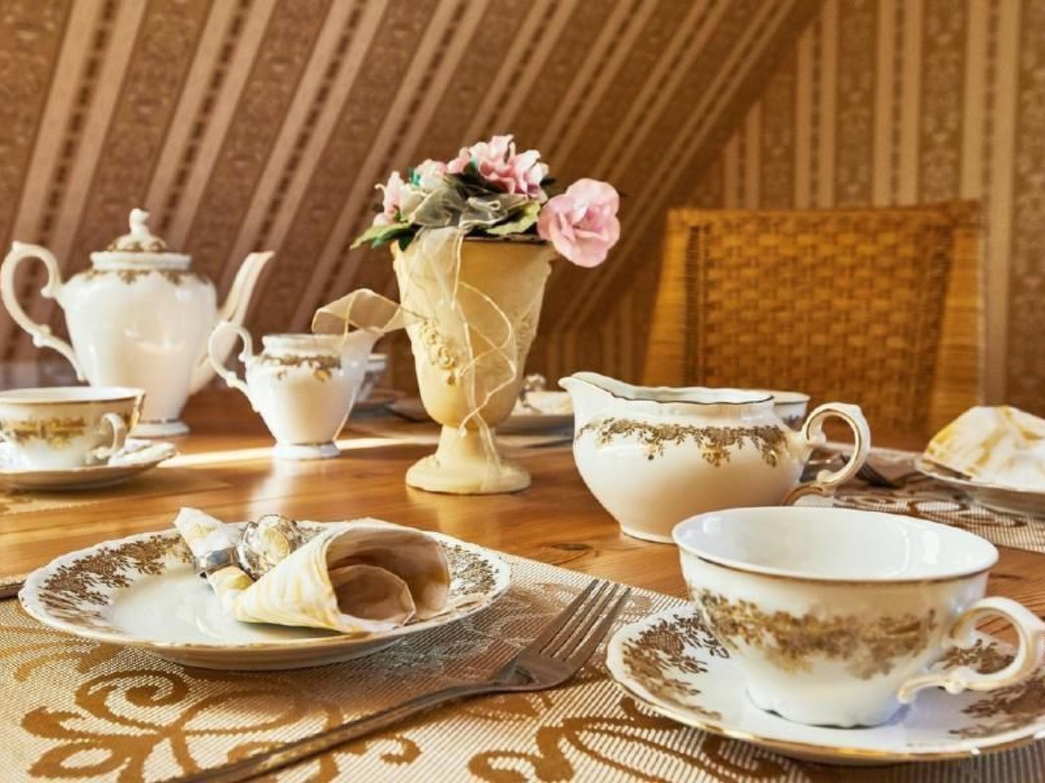 Une table à manger dressée avec un service à thé ancien, comprenant des théières, des tasses et un vase rempli de fleurs.