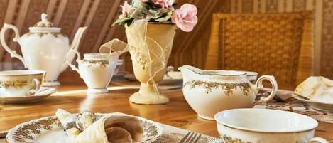 Una mesa de comedor dispuesta con vajilla de té antigua, incluyendo teteras, tazas y un florero con flores.