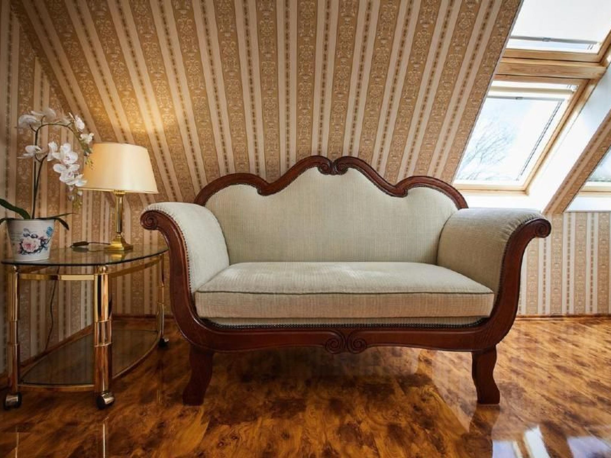 Ein altes Sofa in einem Raum mit Streifenmuster-Tapete und Holzboden.