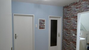 Un couloir avec deux portes blanches, un tableau accroché au mur et un mur à texture.