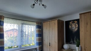 Une chambre à coucher avec un lit, une armoire en bois, une fenêtre avec des rideaux et un tableau représentant un lion accroché au mur.