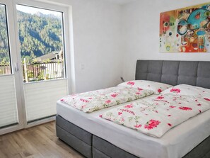 Une chambre avec un lit, une vue sur un balcon accessible par une porte coulissante, et un tableau accroché au mur.