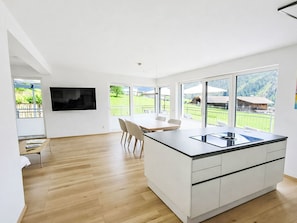 A modern kitchen with a large island, a dining area with chairs, and a TV mounted on the wall. - Vacation home  by Interhome (Arnbach)