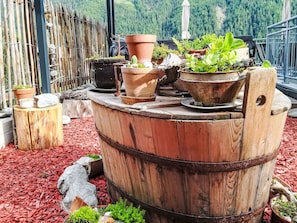 A wooden barrel used as a planter with various potted plants on top, surrounded by red mulch and rocks. - Vacation home  by Interhome (Arnbach)