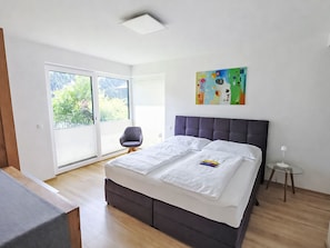 A modern bedroom with a large bed, a chair, a small table, and a painting on the wall. - Vacation home  by Interhome (Arnbach)