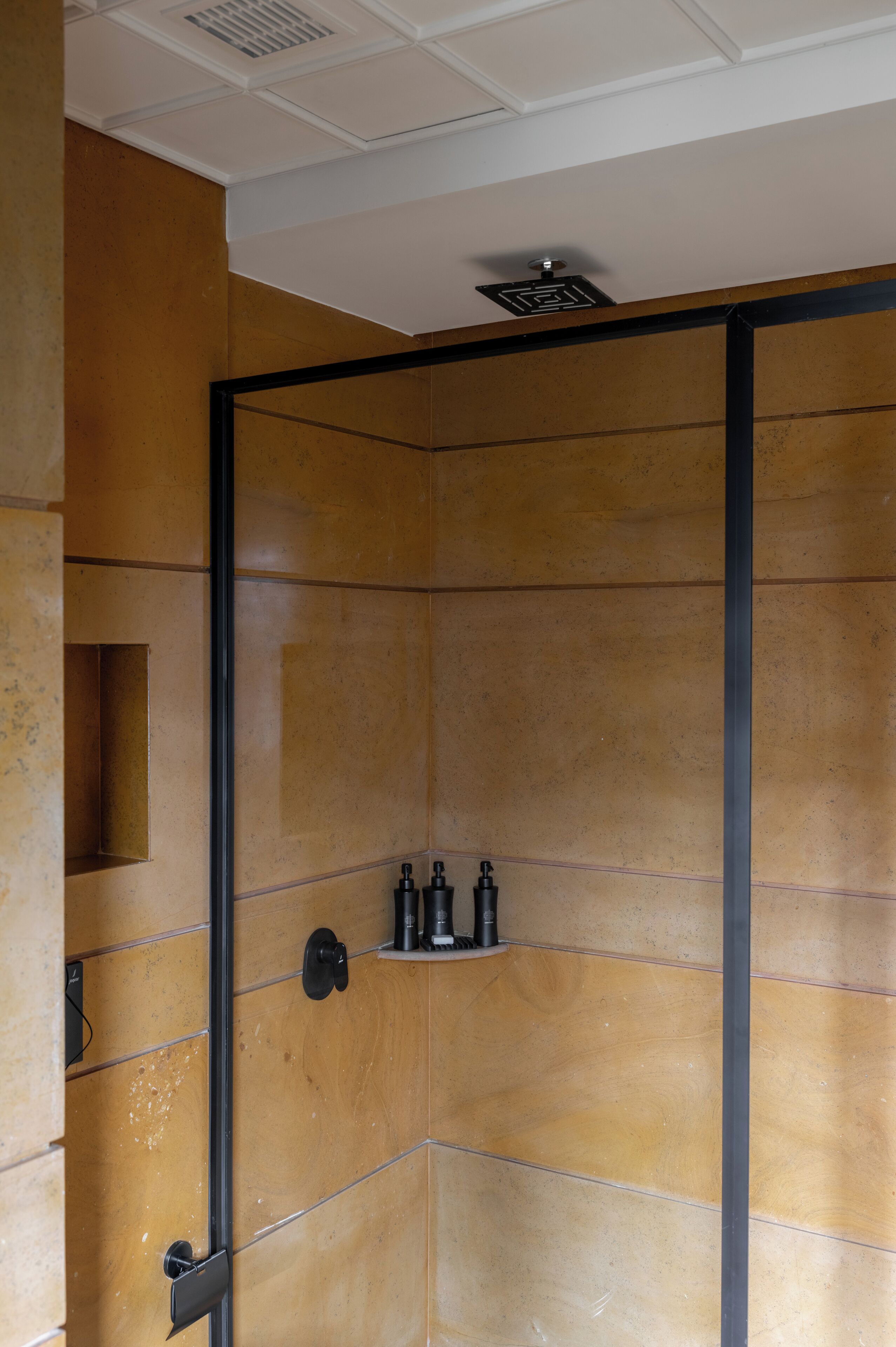 A modern bathroom with a wooden wall design, a black door, and a shelf with toiletries.
