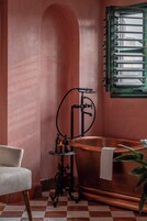 A bathroom with a copper bathtub, a small table with candles, and a chair.