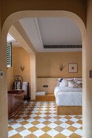 A hotel room with a checkered floor, a bed with white bedding, a bathtub, and a wall-mounted light fixture.