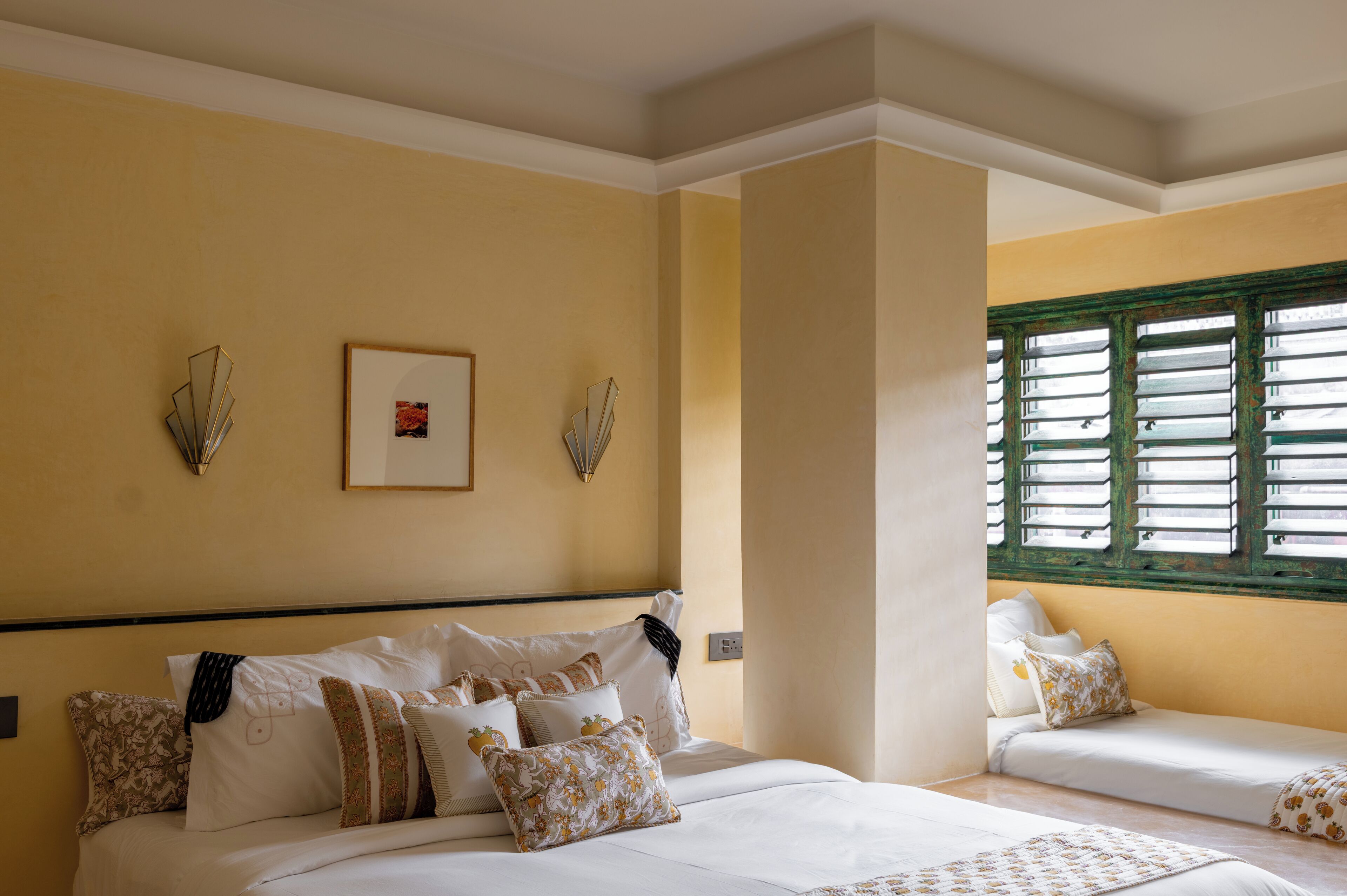 A hotel room with a bed, a window with shutters, and a wall-mounted light fixture.