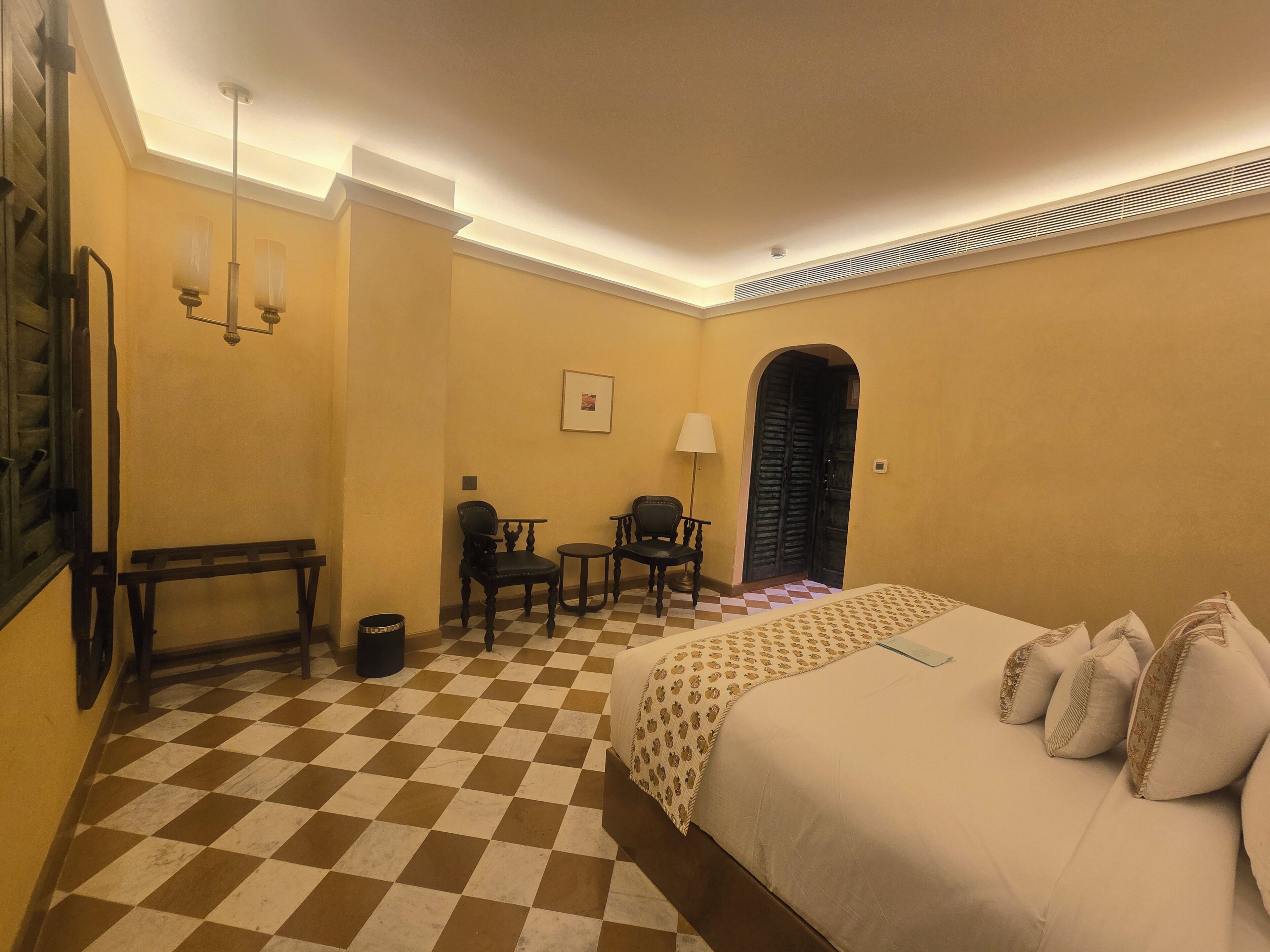 Habitación de hotel con piso a cuadros, cama con almohadas, escritorio con silla y lámpara.