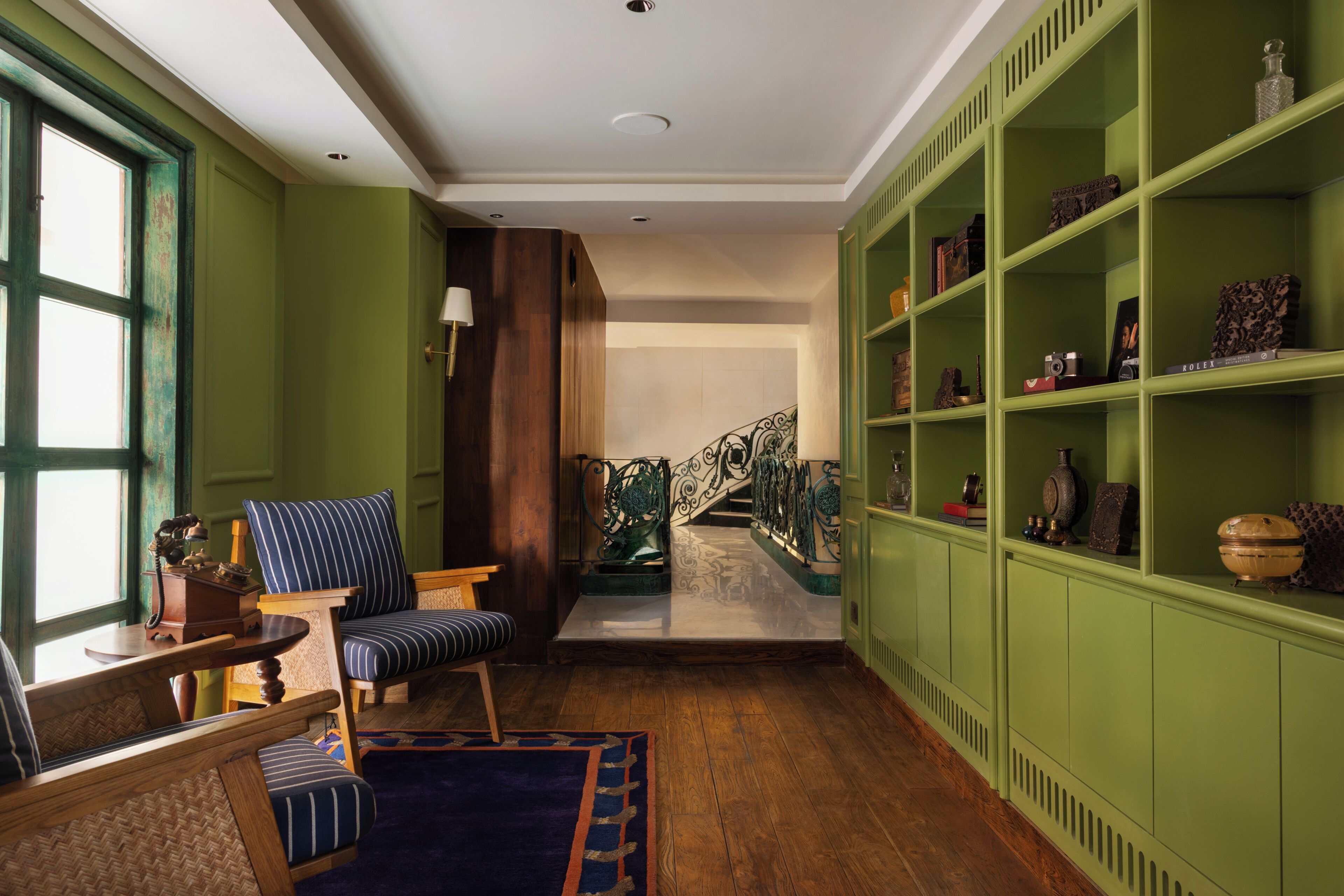 Una habitación con piso de madera, una escalera, un estante verde y sillas tapizadas a rayas.