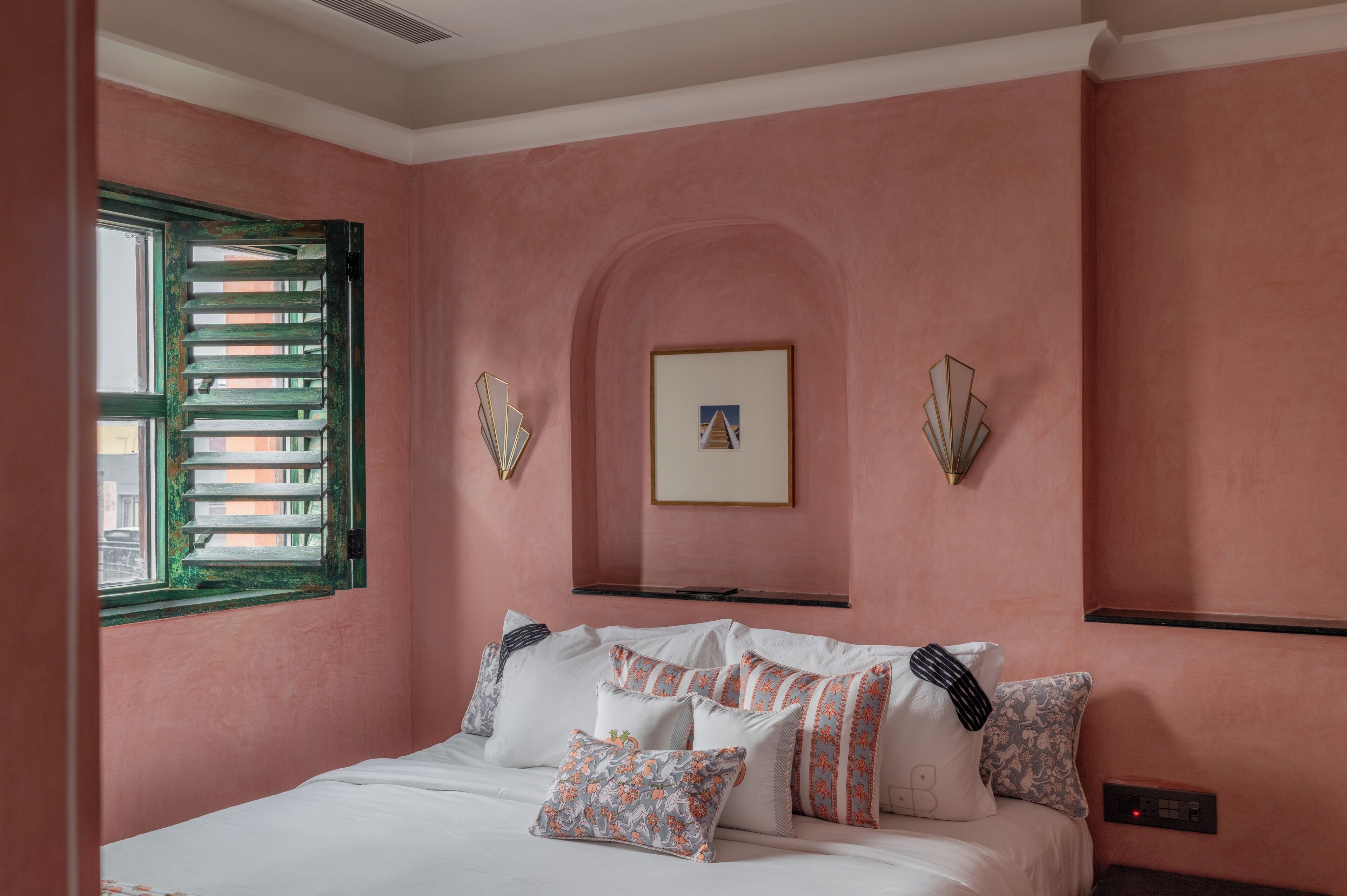 Une chambre à coucher avec un lit, des oreillers, un tableau encadré et une fenêtre avec des volets.