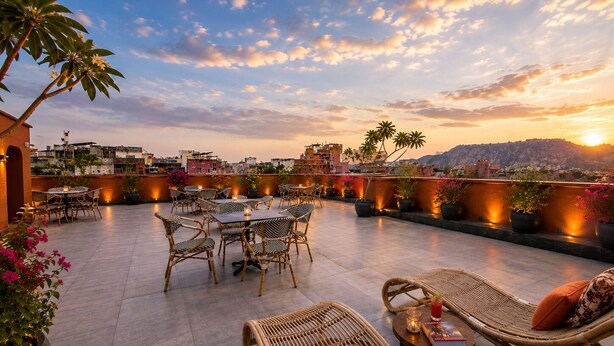 A rooftop terrace with wicker furniture, potted plants, and a sunset view. - Abode Jaipur (Jaipur)