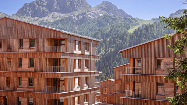 Un edificio de madera de varios pisos con balcones, con montañas al fondo.