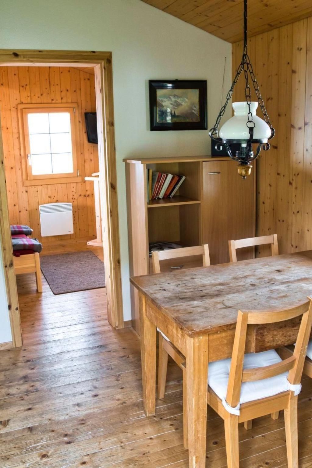 Un intérieur en bois comprenant une table à manger, des chaises, une bibliothèque et un luminaire suspendu.