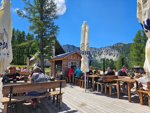 An outdoor seating area with wooden benches and tables, surrounded by mountains and trees. - Haus Petzenblick by Interhome (Gonowetz)