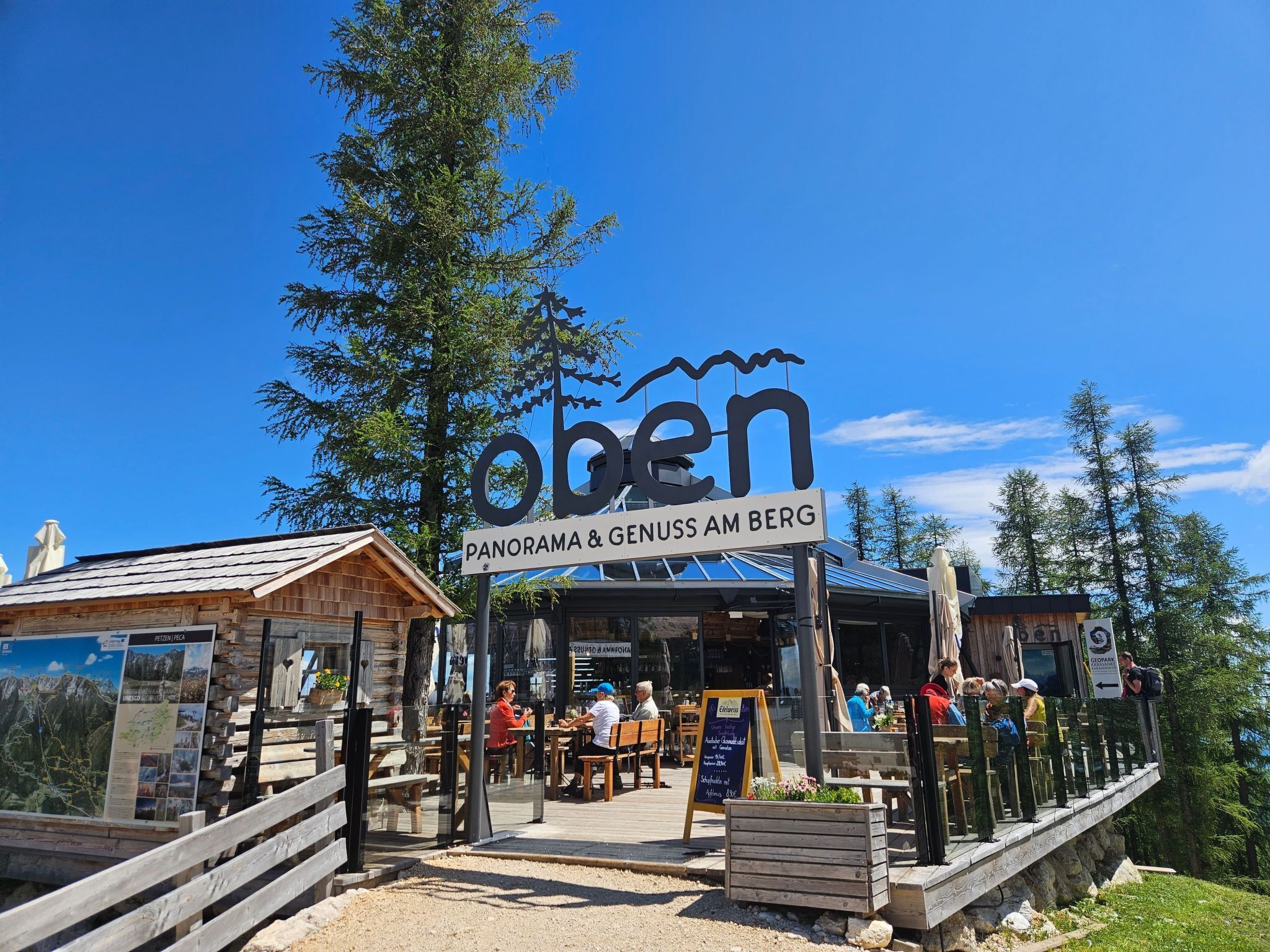Un ristorante chiamato "Oben Panorama & Genuss am Berg" con tavoli all'aperto e vista sulle montagne.