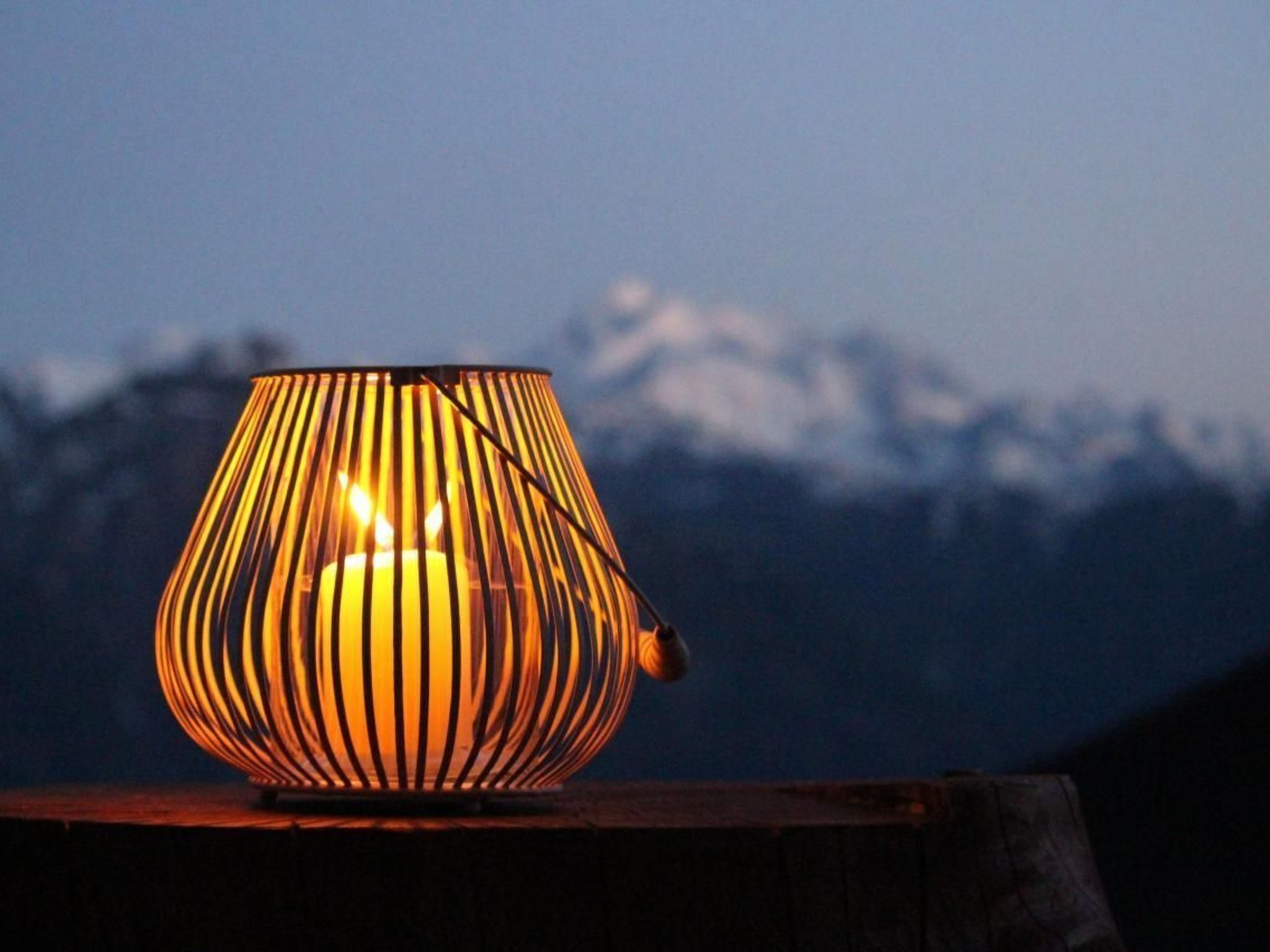 Ein Kerzenhalter mit Streifenmuster auf einer Holzoberfläche vor einer Bergkulisse.