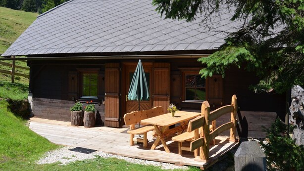 A wooden cabin with a sloped roof, a wooden deck, and a table with benches. - Guglhütte by Interhome (Reichenfels)
