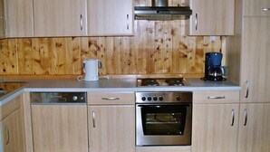 A compact kitchen with wooden cabinets, a dishwasher, a stove, and an oven. - Guglhütte by Interhome (Reichenfels)