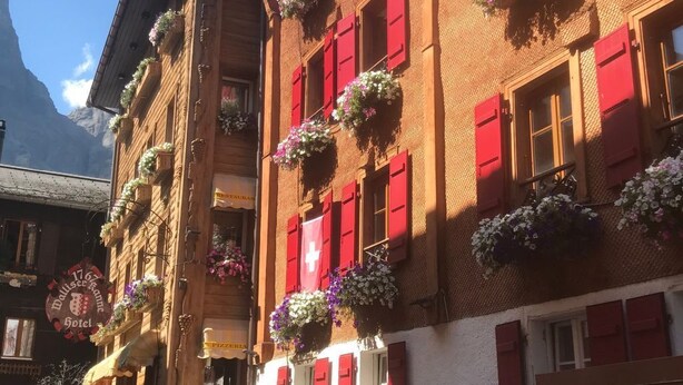 Un edificio tradicional europeo con contraventanas rojas y jardineras con flores, que cuenta con un restaurante y un letrero de hotel.