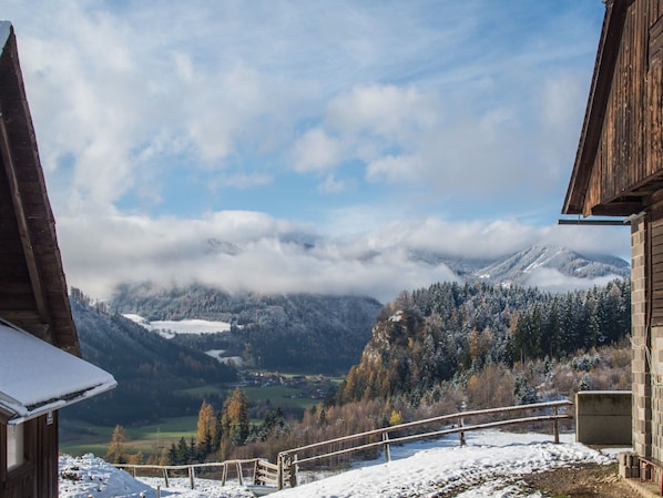 A wooden cabin with a view of snow-covered mountains and a valley.