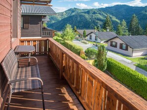 A wooden balcony with wicker furniture, overlooking a residential area and mountains.