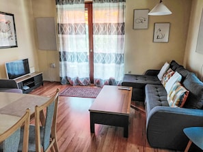 A living room with a sofa, a coffee table, a TV, and a dining area with a table and chairs.